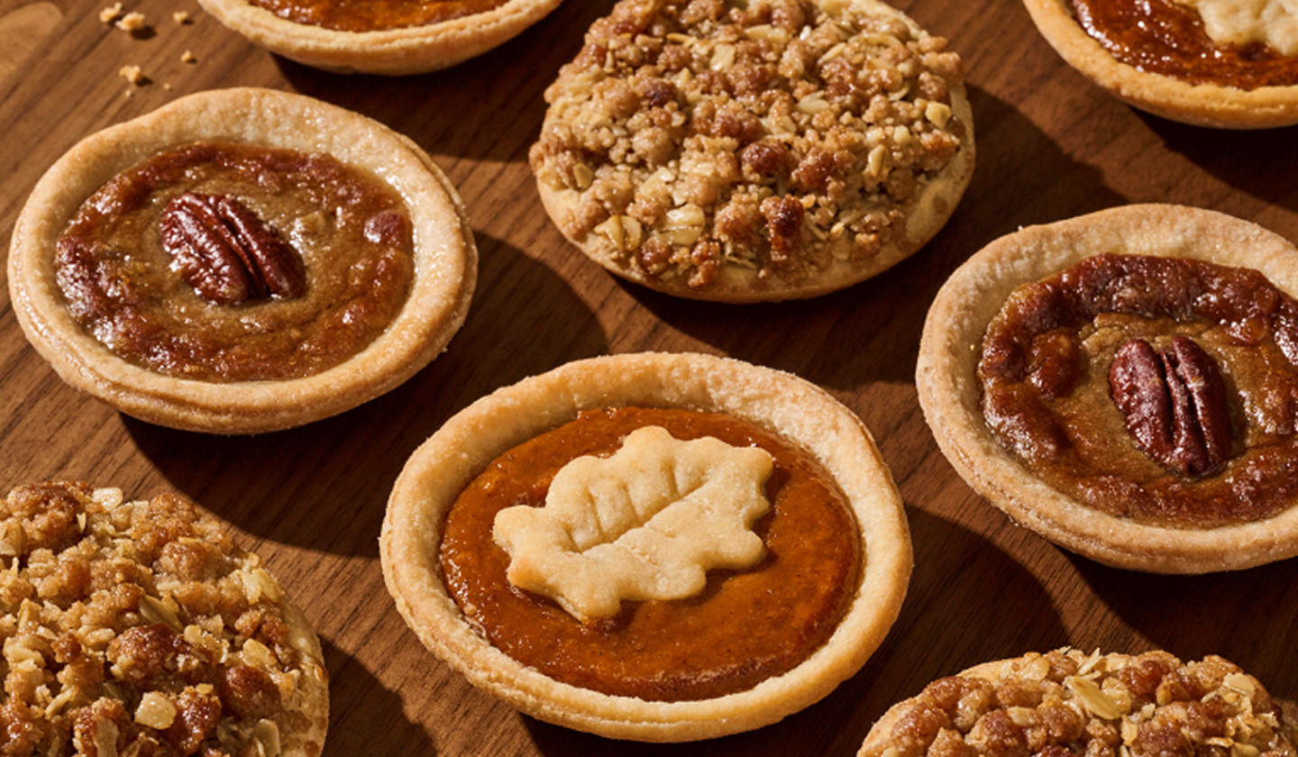 A variety of mini pies grouped together on a wood table.